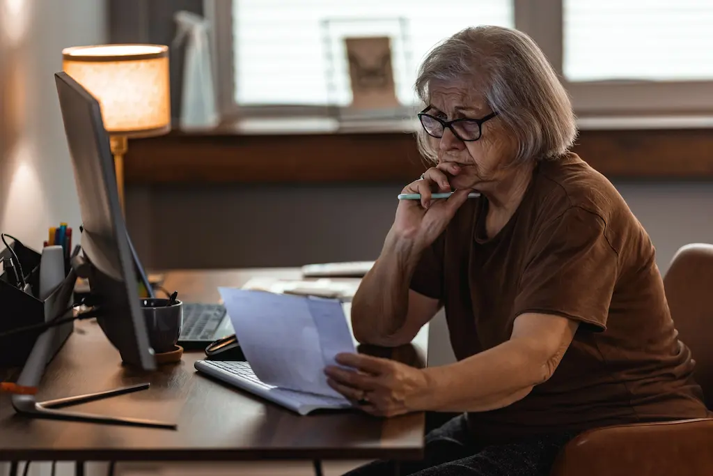 Senior reviewing financial documents with concern/stress